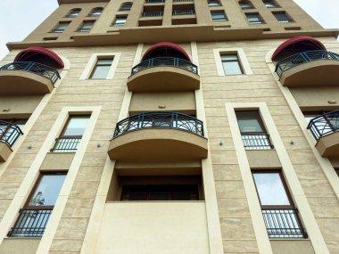 Yapının kırmızı tenteleri olan birkaç balkonları vardır. Pürüzsüz bir taş yüzüyle dimdik ayakta duruyor. Öğlen oldu ve hava açık..