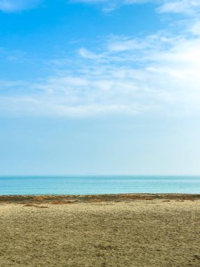 Öğleden sonra erken saatlerde mavi gökyüzünün altında yumuşak kum ve berrak su bulunan bir sahil manzarası. Ufuk, denizin gökyüzüyle uzak bir çizgide buluştuğu yeri gösteriyor..