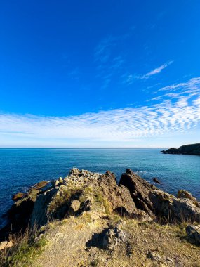 İki kayalık uçurum, berrak mavi su ve parlak gökyüzü ile geniş bir okyanus manzarasına sahiptir. Sahne gün ışığında sahilin doğasının güzelliğini gösteriyor..