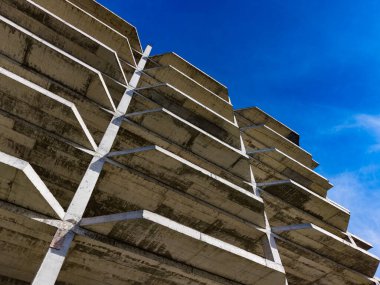 Mavi gökyüzüne karşı yükselen beton bina yapısına sahip inşaat alanı. Konferansta binanın iskeleti ve destek sütunları ele alınıyor.