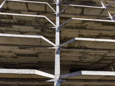 Beton bir binanın iskeleti aşağıdan görülebilir. Yapının birçok seviyesi ve gri betondan yapılmış yatay ve dikey kirişleri vardır..