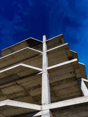 Beton yapı, belirgin katmanları ve parlak mavi gökyüzünün altında destekleriyle yüksek duruyor. Bu ayar kentsel gelişimin özünü yakalar.