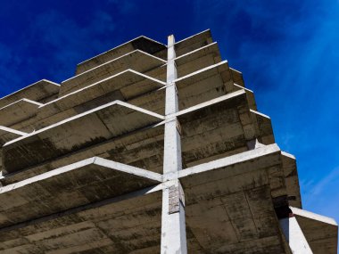 İşçiler inşaat alanında beton bir yapı inşa ediyorlar. Manzara yükselen iskeleti gösteriyor. Gün ortasında gökyüzü masmavi..