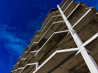 Gökyüzüne doğru uzanan beton yapısı olan bir inşaat alanı. Bu açı, canlı mavi bir arkaplan karşısında birden fazla seviye ve güçlü çizgiler görüntüsü sunar..