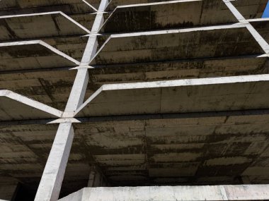 İnşaat halindeki beton bir binanın manzarası. Yapıyı destekleyen sütunlar ve katlar üzerinde duruluyor. Hava açık olan bir şehir alanı..