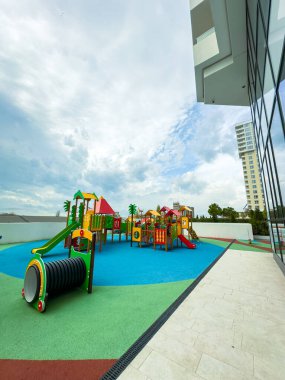 Çocuk parkında, açık alan ve bulutlu gökyüzü altındaki modern binalarla çevrili bir çatıda çeşitli yapılar ve slaytlar yer alıyor..