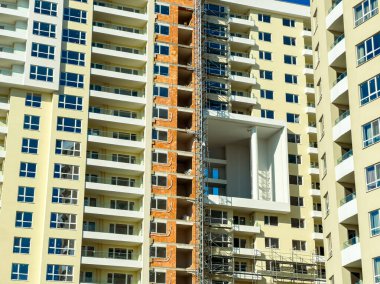 İnşaat işçileri kentteki bir apartmanda çalışmaya devam ederken inşaat iskelesinde çalışıyorlar. Binanın birkaç katı ve birçok penceresi var..