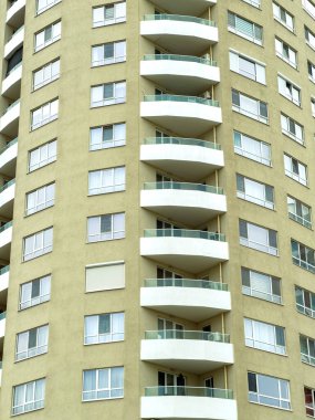 Yüksek bina yapısı birkaç tane yuvarlak balkon gösteriyor. Pencereler gün ışığını yansıtır. Bazı balkonlar boş, bazılarında ise görünür eşyalar var..