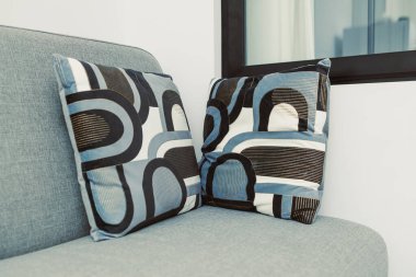 Basit bir yaşam alanındaki gri bir kanepede iki desenli yastık dinleniyor. Yastıklar, oturma düzenine detay ekleyerek renk ve şekillerin bir karışımını gösterir.