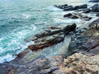Öğleden sonra bir kıyı bölgesindeki kayaların üzerinden su sıçrıyor. Dalgalar oluşup taşlara çarpar ve okyanusta dalgalanmalar yaratır..