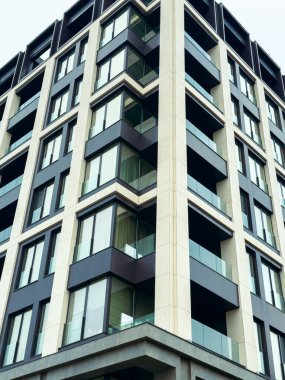 Yapı birden fazla katlı yüksek bir bina gösteriyor. Büyük cam pencereler ve balkonlar çağdaş bir görünüm yaratıyor. Bu şehir sahnesinde bulutlu gökyüzü arka planı oluşturur..