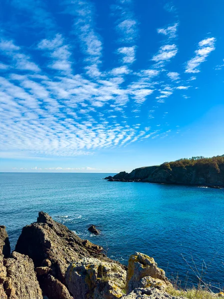 Bulutlu mavi gökyüzü açık okyanusun yanındaki kayalık bir kıyı şeridinin üzerindedir. Dalgalar kayalara çarpar ve sahne suyun kenarında sakin ve güneşli bir gün gösterir..