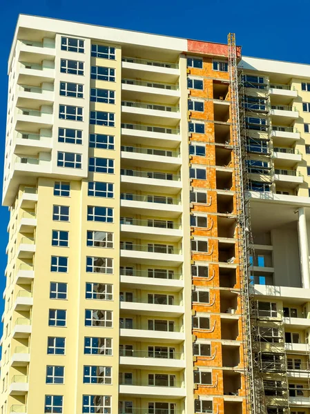 İşçiler, açık gökyüzü ve parlak güneş ışığına sahip kentsel alanda yapım aşamasındaki yüksek katlı bir binanın dış cephesine malzeme yerleştiriyorlar..