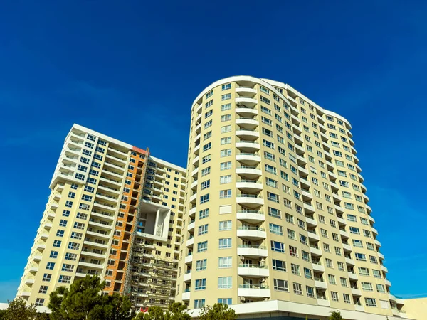 Kentsel bir bölgede mavi gökyüzüne yükselen iki yüksek bina. Güneş parlıyor, mimariyi aydınlatıyor ve çevresindeki yeşillikleri aydınlatıyor..