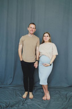 Bir çift yan yana durur, gülümser ve el ele tutuşur. Kadının görünen bir bebek yumrusu var ve açık renk bir bluz ve etek giyiyor. Düz tişörtlü ve siyah pantolonlu adam onun yanında duruyor..