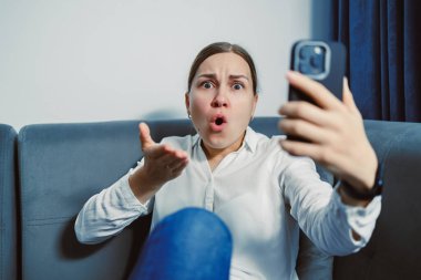 Evdeki koltukta oturan bir kadın telefonunu tutarken şaşkın şaşkın bakıyor. Görünür bir şok ve güvensizlik ifadesiyle bir sohbete daldı..