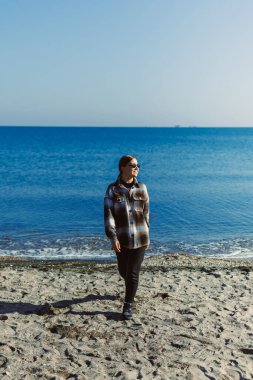 Bir insan açık gökyüzünün altında suyun kenarındaki kumda gezinir. Deniz sakin, ve ışık dalgalardan yansıyor. Sahne parlak ve sıcak görünüyor..