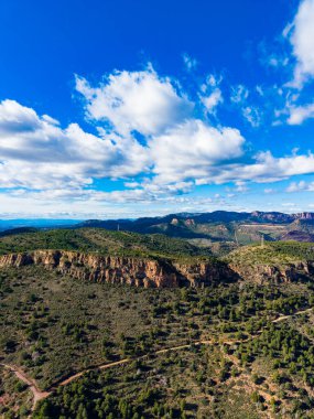 Sahne, parlak mavi gökyüzünün altında beyaz bulutlarla kaplı ağaçlarla kaplı yuvarlanan tepeleri gösteriyor. Manzara gün boyunca yüksek bir noktadan alınır. Manzara uçsuz bucaksız ve el değmemiş görünüyor.