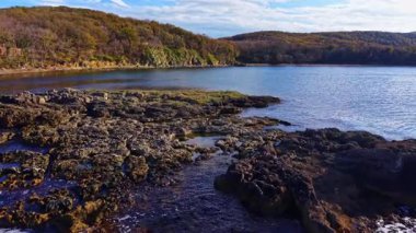 Sıcak güneş ufukta belirdiğinde sakin sular engebeli bir sahili kucaklıyor. Bereketli sonbahar yaprakları tepeleri taçlandırır, barışçıl ve doğal bir geri çekilme yaratır..