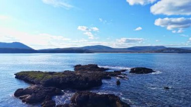 Parıldayan dalgalar, güneş parlarken engebeli kayalara çarpar. Yuvarlanan tepeler ve uzak dağlar, resmedilmeye değer kıyı manzarasını çerçeveletip, bir huzur hissi yaratıyor..