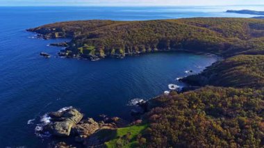 Engebeli kayalıklarla canlı ağaçlar arasında yuva yapmış sakin bir koy, ziyaretçileri sakin sularını keşfetmeye davet ediyor..