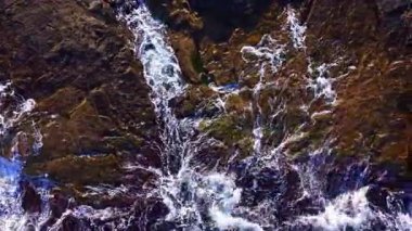 Dalgalar eski kayaların etrafında dalgalanır ve suyun karayla buluştuğu çarpıcı bir manzara yaratır. Güneş uzaklardan batıyor, engebeli yüzeye altın renkler döküyor..