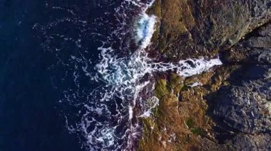 Günbatımının ılık tonlarının altında, güçlü dalgalar dalgalı kayalıklarla buluşur, havaya su püskürtür ve denizin kenarında doğal bir manzara yaratır..