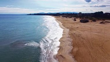 Yumuşak dalgalar, parlak güneşli gökyüzünün altında uzanan altın kumun olduğu kıyıya nazikçe uzanır. Sakin okyanus ışığı yansıtır, sakin bir sahil manzarası yaratır..