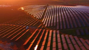 Güneş panellerinin sıraları, güneş batarken pırıl pırıl parlayarak araziye yayılıyor. Sıcak turuncu ve altın renkler, sürdürülebilir enerjinin hareket halinde nefes kesici bir görüntüsünü oluşturur..