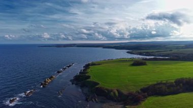 Yuvarlanan yeşil tepeler, bulutlar tembelce üzerimizde sürüklenirken sakin mavi denizle buluşur. Doğanın kıyı şeridiyle uyum içinde büyüdüğü sakin bir manzara yaratır..