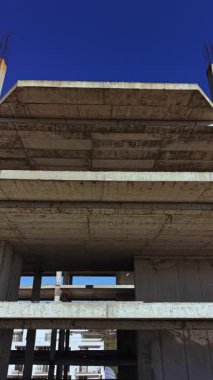 Çok katlı beton bir bina, canlı bir şehir ortamında, canlı bir mavi gökyüzünün hammadde ve iskeletini vurgulayarak, canlı bir mavi gökyüzüne karşı şekil alır..