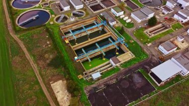 Hava görüntüsü bir su arıtma tesisinin düzenli kısımlarını yakalıyor. Havuzlar ve makineler gün ortası güneşinin altında uyumlu bir şekilde çalışıyor ve herkes için güvenli su sağlıyor..