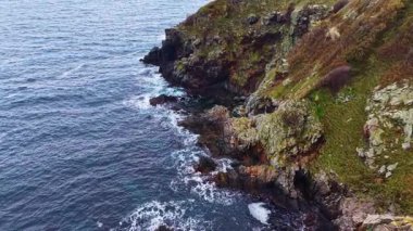 Güneş, canlı yeşilliklerle bezenmiş uçurumların ardında batarken dalgalar yavaşça kayalık kıyılara vuruyor. Huzurlu bir atmosfer kıyı sahnesini sarar, yansıma ve sükuneti davet eder..