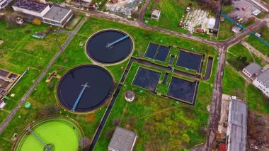 Hava görüntüsü dairesel ve dikdörtgen tankları olan bir su arıtma tesisi gösteriyor. Bölgedeki tanklar ve binalar yeşil çimlerle çevrili. Kompleksin içinden geçen bir yol.