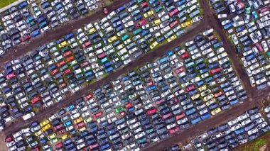 Bir hurdalık sıra sıra dizilmiş birçok park edilmiş araçlarla doludur. Sahne farklı renk ve boyutlarda arabaları gösteriyor. Bazı araçlar hasar görürken, diğerleri açık gökyüzünün altında el değmemiş görünüyor..