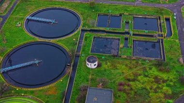 Atık su arıtma tesisi yukarıdan gösteriliyor. Geniş dairesel tanklar su tutarken çeşitli işleme birimleri görülebilir. Kentsel bir ortamda altyapıyı çevreleyen yeşil alanlar.