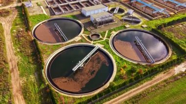 Su arıtma tesisindeki dairesel tanklar bulanık suyla doludur. Bu da süregelen arıtma sürecini gösterir. Yakındaki sanayi binaları, güpegündüz yemyeşil tarlalarla çevrili..