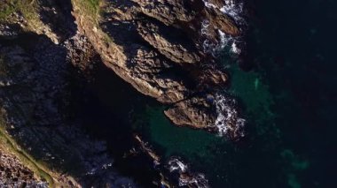 Sarsıcı uçurumlar, dalgaların sivri kayalara çarptığı turkuaz bir denizden keskin bir şekilde yükselir. Güneşin yansımaları parıldıyor, nefes kesen bir kıyı manzarası yaratıyor..