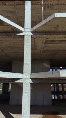 Beton kirişler ve sütunlar parlak mavi gökyüzünün altında çarpıcı bir bileşim oluşturarak, açık bir manzaradaki bitmemiş yapının cesur mimari unsurlarını vurguluyor..