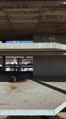 Uçsuz bucaksız, boş bir uzay, sert beton sütunlar ve boş zeminler sergiliyor. Güneş ışığı boşluklardan akıyor, kumlu zeminde uzun gölgeler bırakıyor..