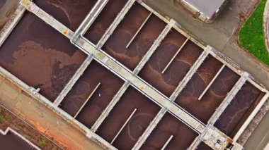 Koyu sıvı ile dolu büyük havuzlar atık su tedavisinin ileri safhalarını gösteriyor. Endüstriyel yapılar, suyun dolaştığı ve arıtılmaya hazırlandığı geometrik desenler oluşturur..