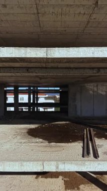 Güneş ışığı bitmemiş bir binayı sular altında bırakır, çıplak beton duvarları ve zemini aydınlatır. Ağır kirişler ve toprak etrafa saçılmış, devam eden inşaat ve kentsel dönüşümü vurguluyor.