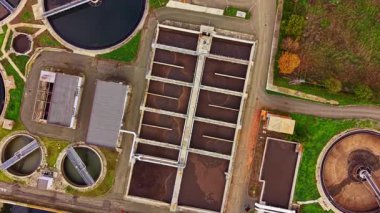 Hava manzarası, açık bir günde yeşil ve mühürlü binalarla çevrili yuvarlak tankları ve dikdörtgen havzaları olan bir atık su arıtma tesisinin organize yapısını gösteriyor..