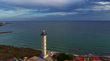 Çarpıcı bir deniz feneri sakin denize bakıyor, büyüleyici bir köyle çevrili. Dalgalar yavaşça sahile çarparken, gökyüzü yumuşak bulutlarla boyanır. Huzurlu bir atmosfer yaratır..