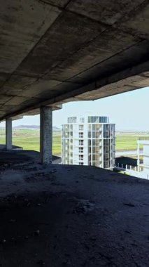 Güneş ışığı, bitmemiş bir yapının iskelet kalıntılarından akar, modern binaların ve ötesinin yemyeşil alanlarının manzarasını çerçeveler. Keşif ve fotoğrafçılık için ideal..