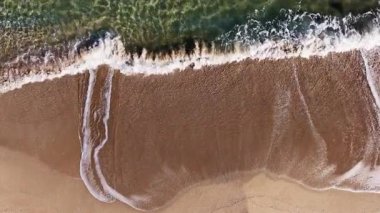 Yumuşak dalgalar kumlu bir plaja yuvarlanarak güneş doğarken köpüklü izler bırakır. Sahnenin sakinliği, doğanın döngülerinin güzelliğini yakalar..