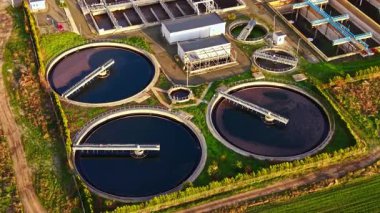 Karanlık suyla dolu dairesel tanklar modern bir su arıtma tesisini işaret ediyor. Yeşil alanlara karşı hazırlanan tesis, güneşli gökyüzünün altında gelişmiş filtreleme teknolojisi sergiliyor..