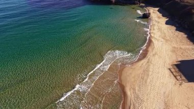 Yumuşak dalgalar kıyıya vuruyor, sakin bir plaj sahnesinde rahatlatıcı bir melodi yaratıyor. Güneş turkuaz sularda parıldıyor, davetkar altın kum ve kayalık araziyi güçlendiriyor..