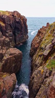 Kıyı boyunca yükselen uçurumlar arasında dar bir kanal kesiliyor. Dalgalar yavaşça kayalık kıyılara vurarak doğal güzelliğin sakin bir manzarasını yaratıyor. Güneş ışığı suda parlıyor..