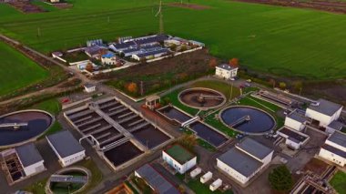 Geniş yeşil tarım arazilerine karşı inşa edilmiş dairesel tankları ve işleme binaları olan bir atık su arıtma tesisinin hava görüntüsü, çevre yönetimini vurguluyor.